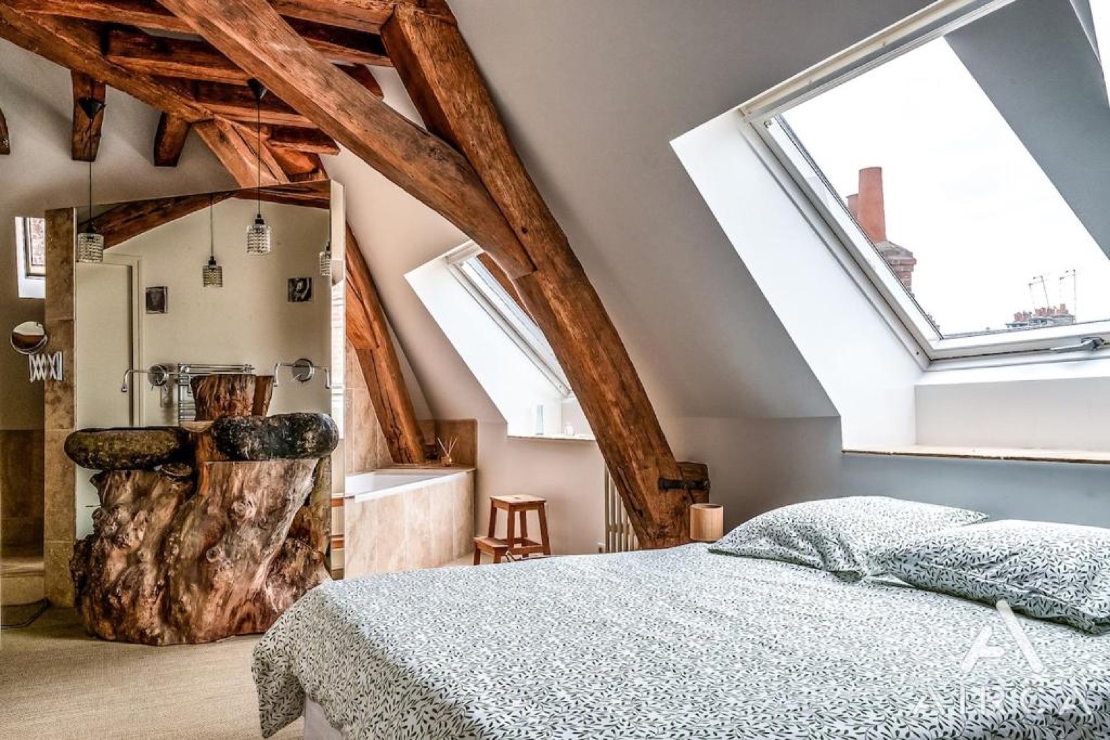 Chambre sous les combles avec charpente apparente et vasque en tronc d'arbre